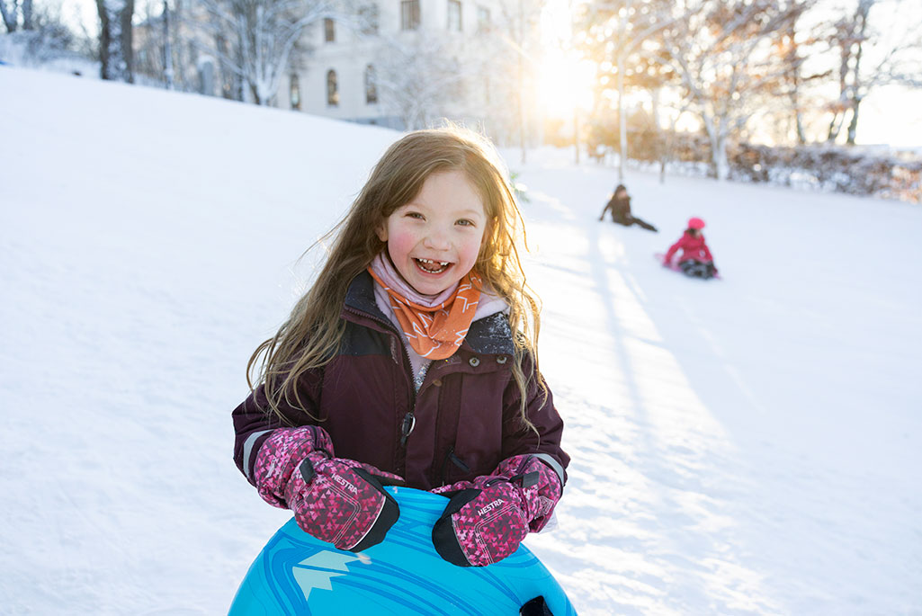 En flicka som håller i en pulka och ler mot kameran utomhus i snön.