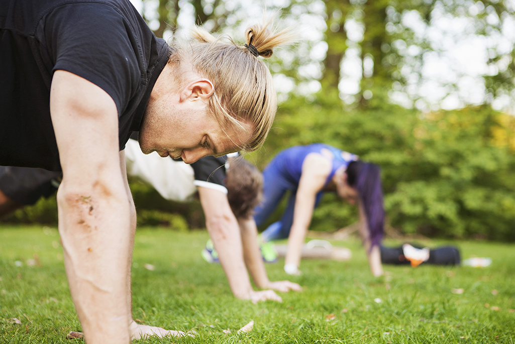 Foto på personer som tränar med kroppsvikt utomhus på en gräsmatta.