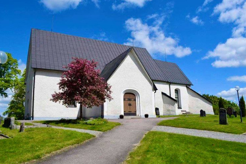 Bild på Villberga kyrka. En vit stenbyggnad med en stor trädörr.