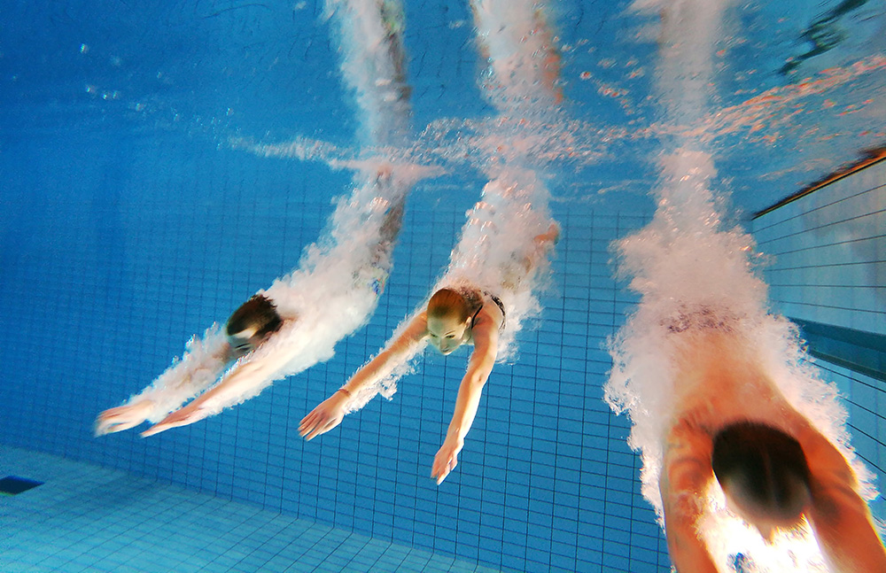 Bild på tre personer som dyker ner i bassängen.